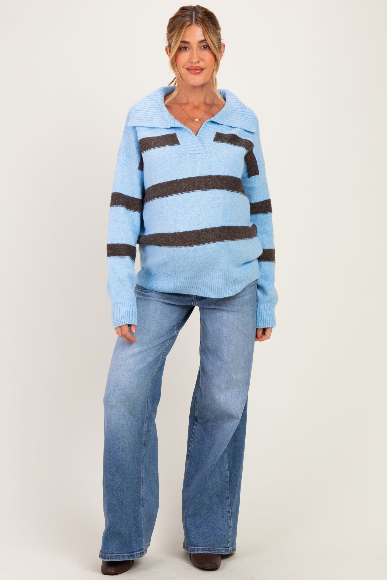 woman wearing a light blue and dark brown striped maternity sweater and blue flared jeans, showing a baby bump