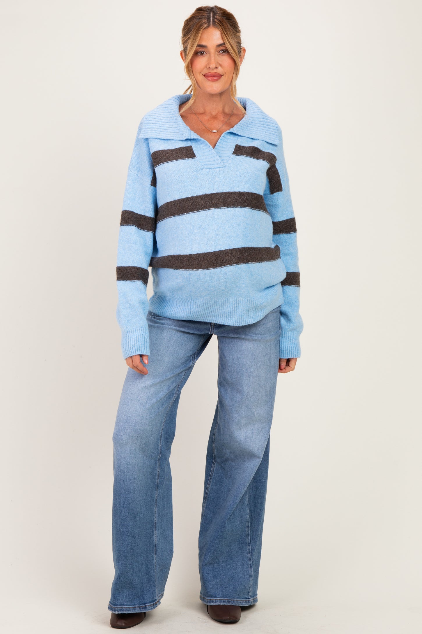 woman wearing a light blue and dark brown striped maternity sweater and blue flared jeans, showing a baby bump