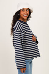 woman wearing a navy and gray striped maternity top, touching her baby bump and smiling, with a white bucket hat