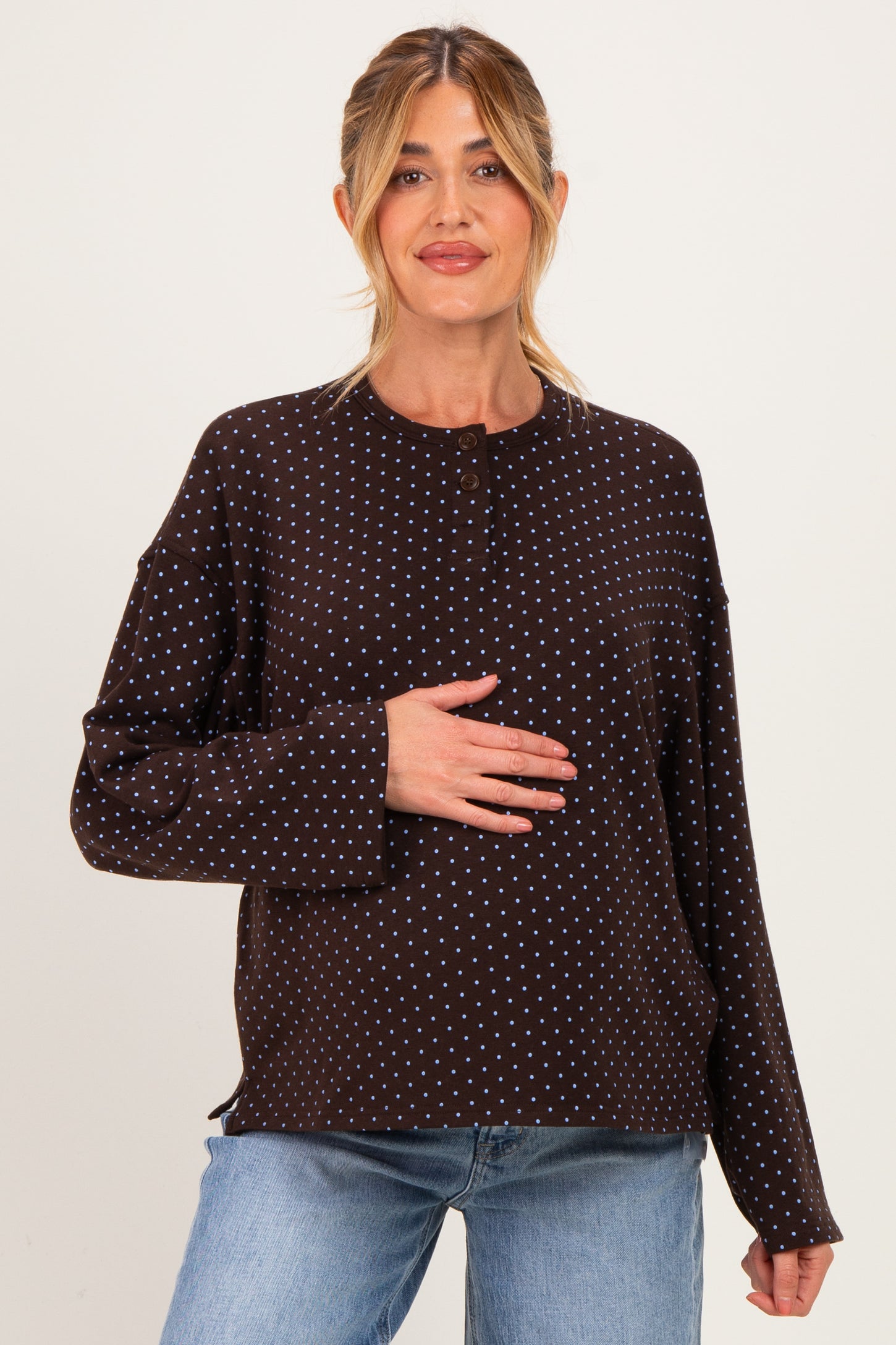 woman wearing a brown polka dot maternity top and holding her baby bump