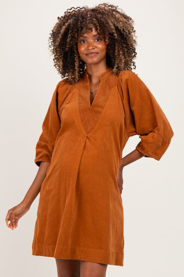 woman wearing a rust-colored corduroy maternity dress with a v-neck and puff sleeves, showing her baby bump