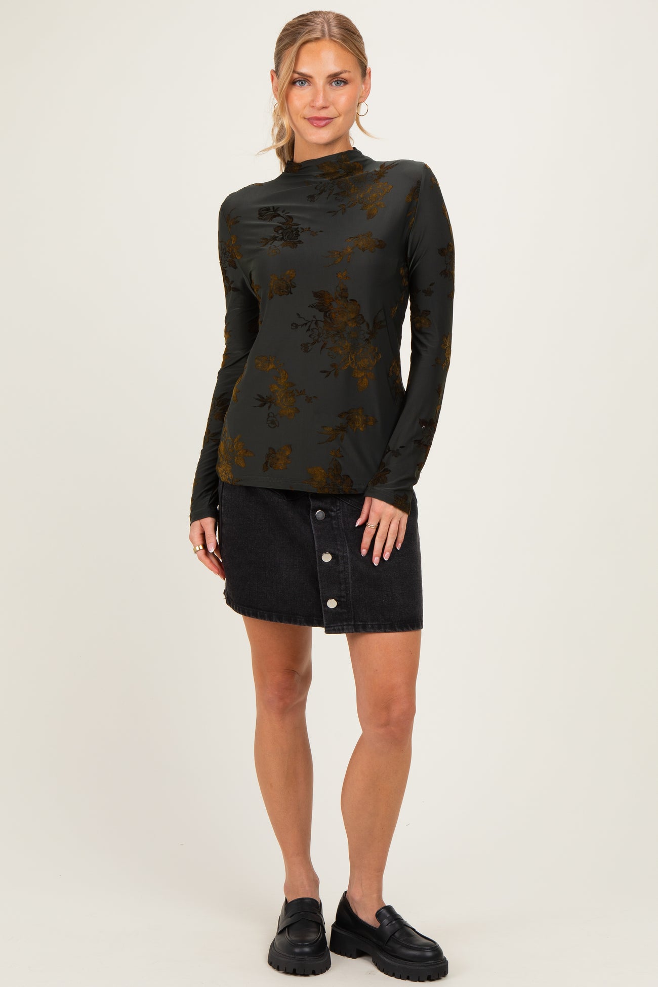 woman wearing a dark green long sleeve top with floral design and a black denim button-up skirt
