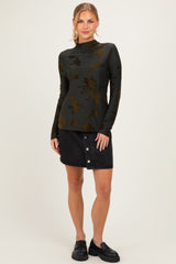 woman wearing a dark green long sleeve top with floral design and a black denim button-up skirt