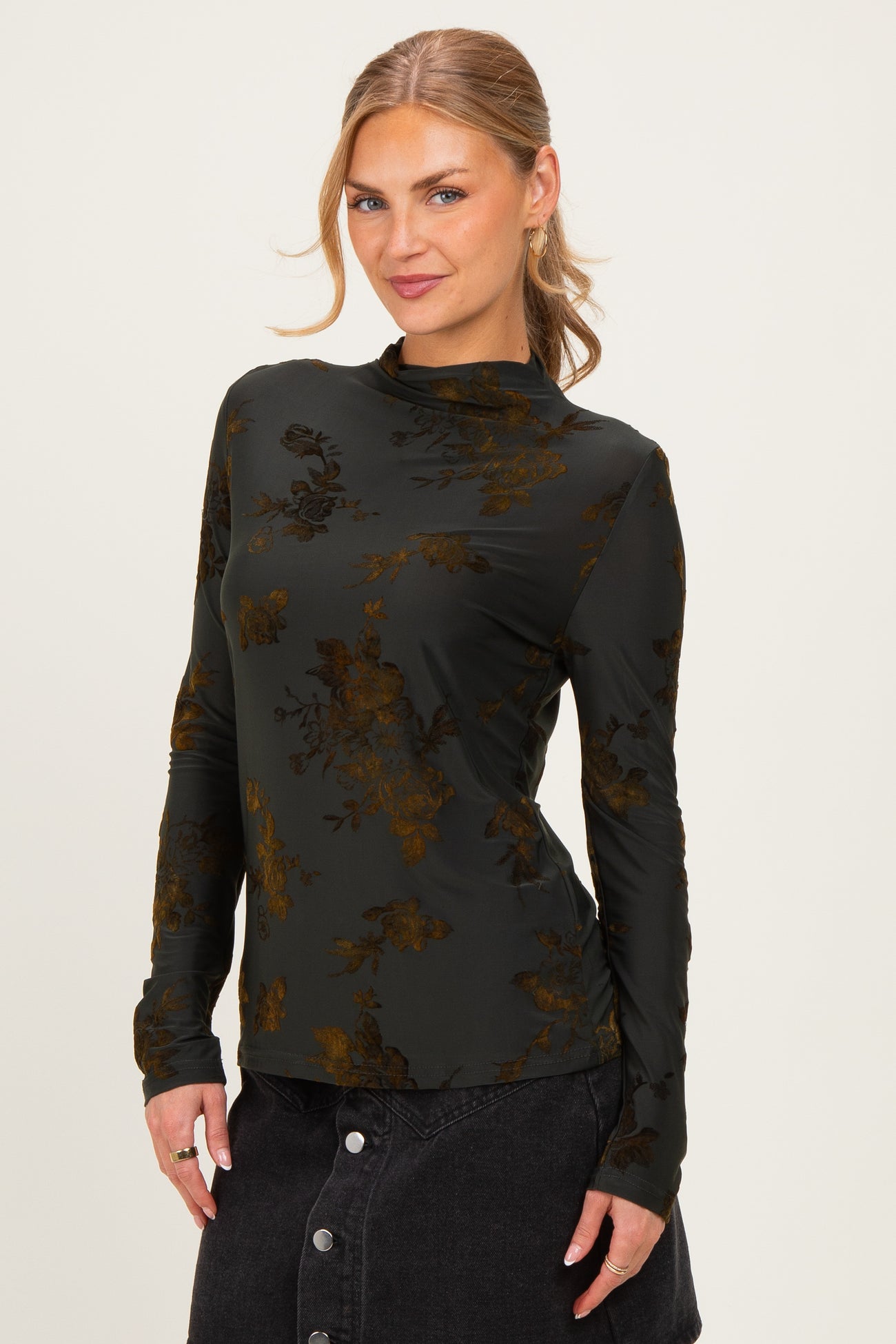 woman wearing a dark green long sleeve top with floral print, posing with a slight smile