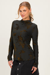 woman wearing a dark green long sleeve top with floral print, posing with a slight smile
