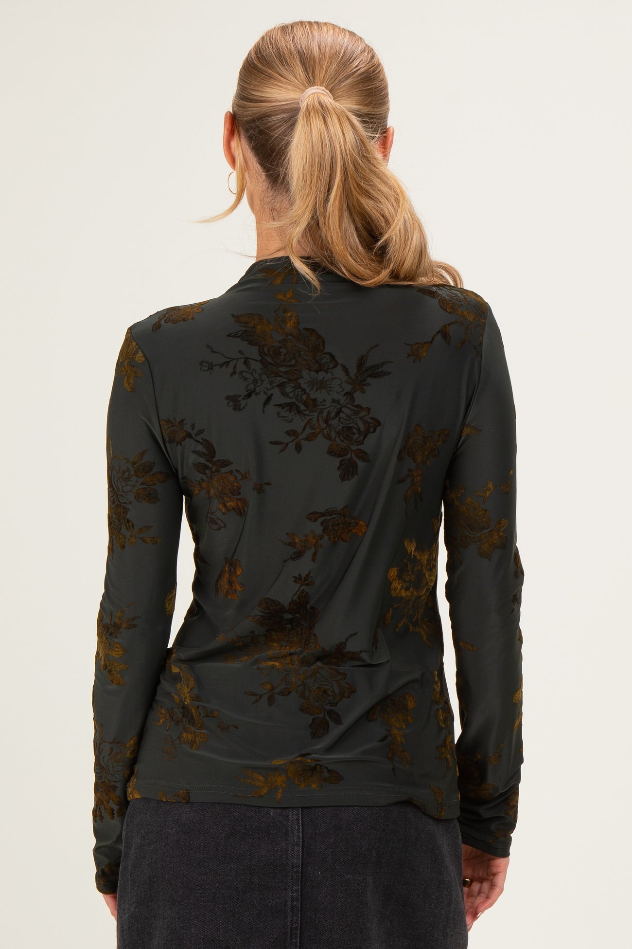 woman wearing a dark green long sleeve top with floral pattern, viewed from the back