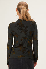 woman wearing a dark green long sleeve top with floral pattern, viewed from the back