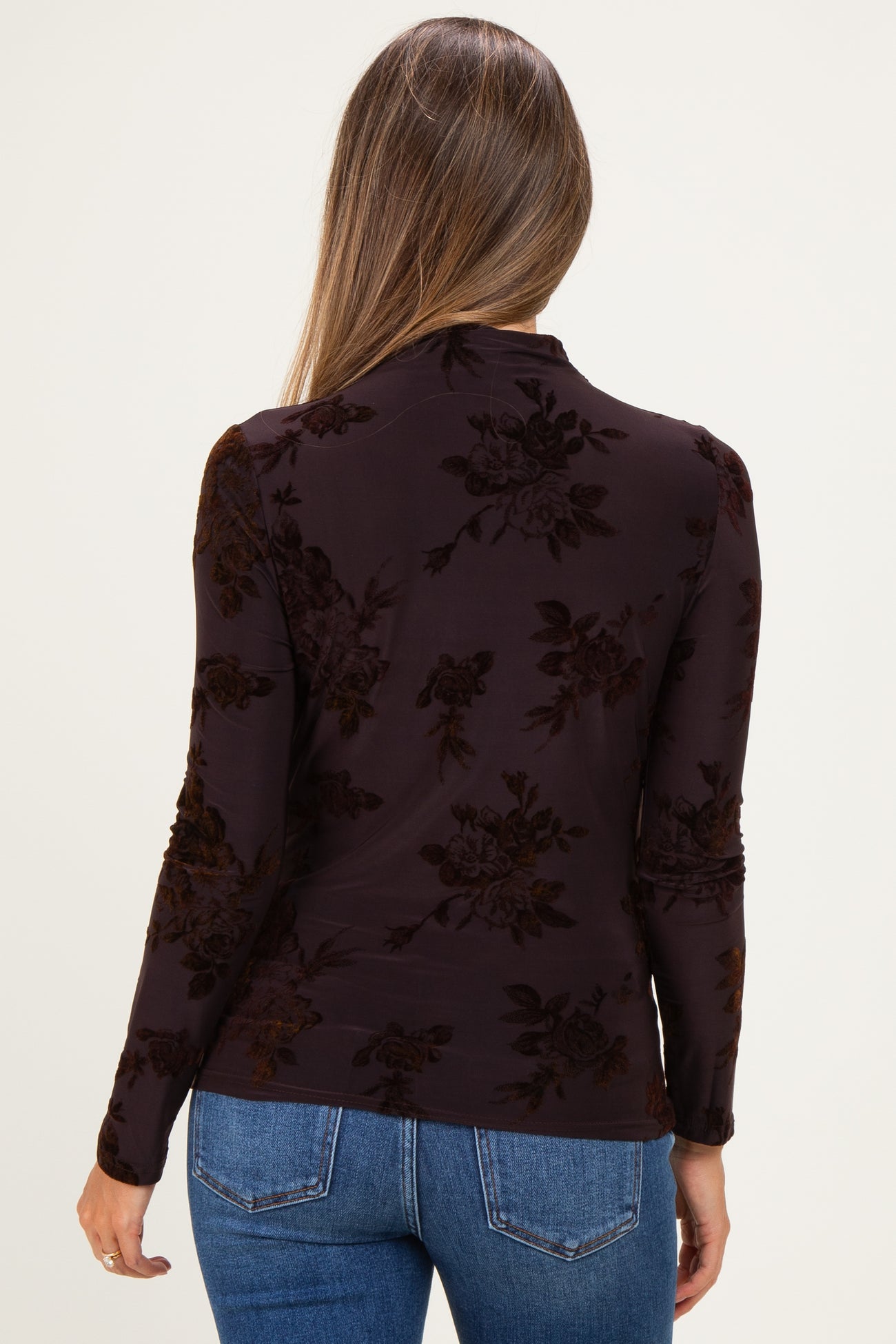 woman wearing a dark floral velvet maternity top, showing the back with styled long sleeves and a fitted design
