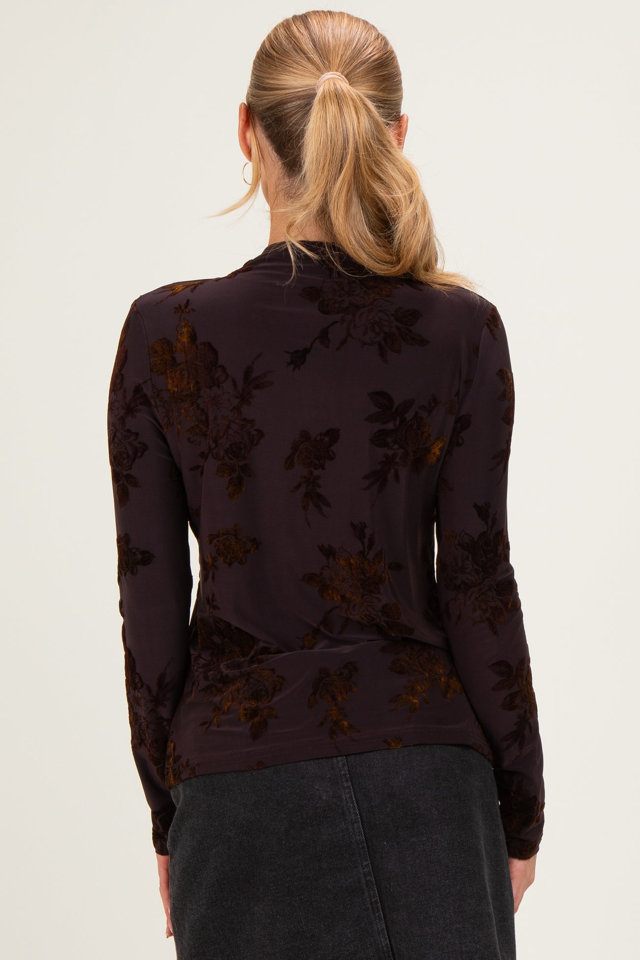 woman wearing a dark floral long sleeve top, seen from the back with a fitted style and subtle texture