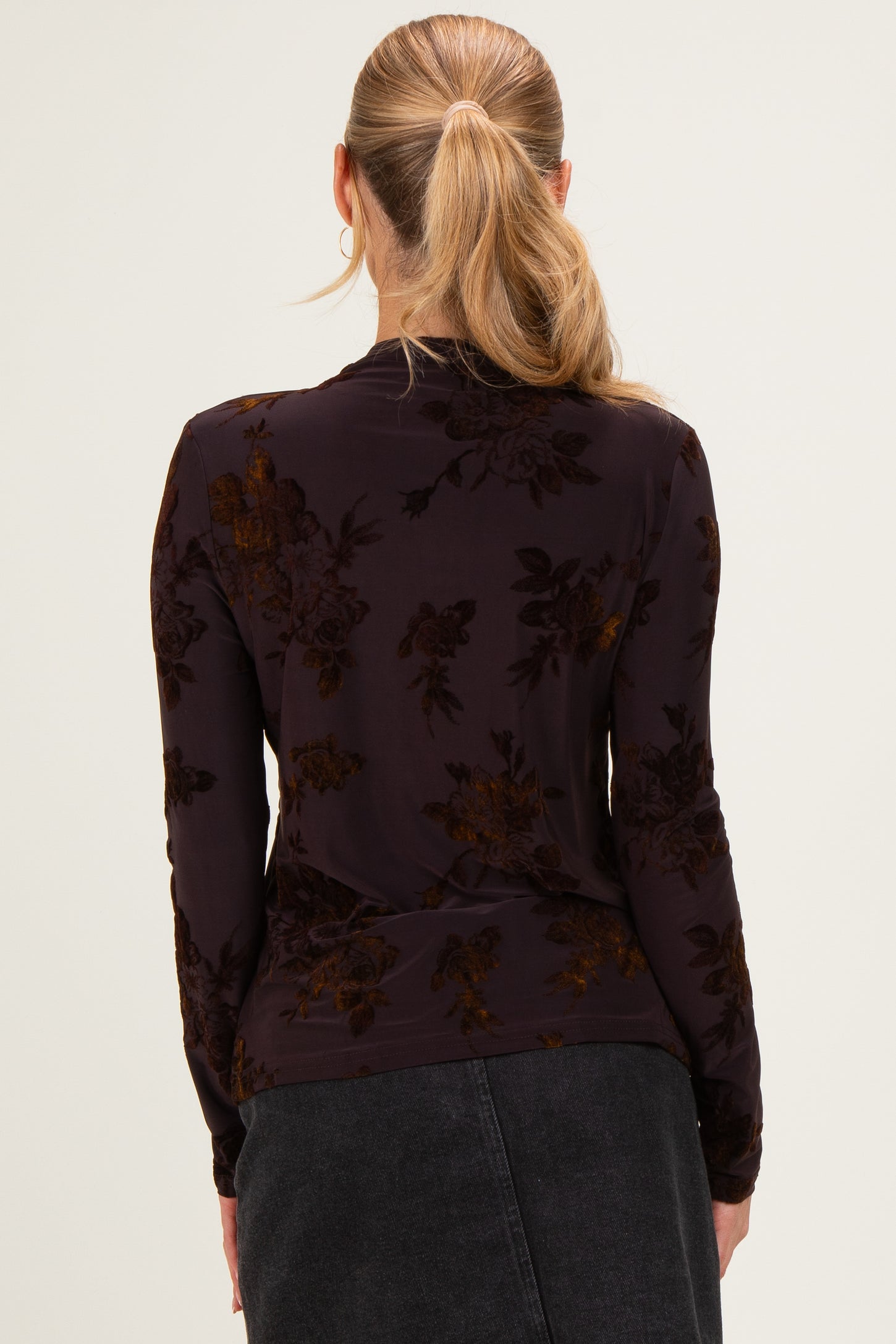 woman wearing a dark floral long sleeve top, seen from the back with a fitted style and subtle texture