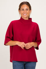 woman wearing a crimson oversized sweater with a high neck and relaxed fit, styled with blue jeans