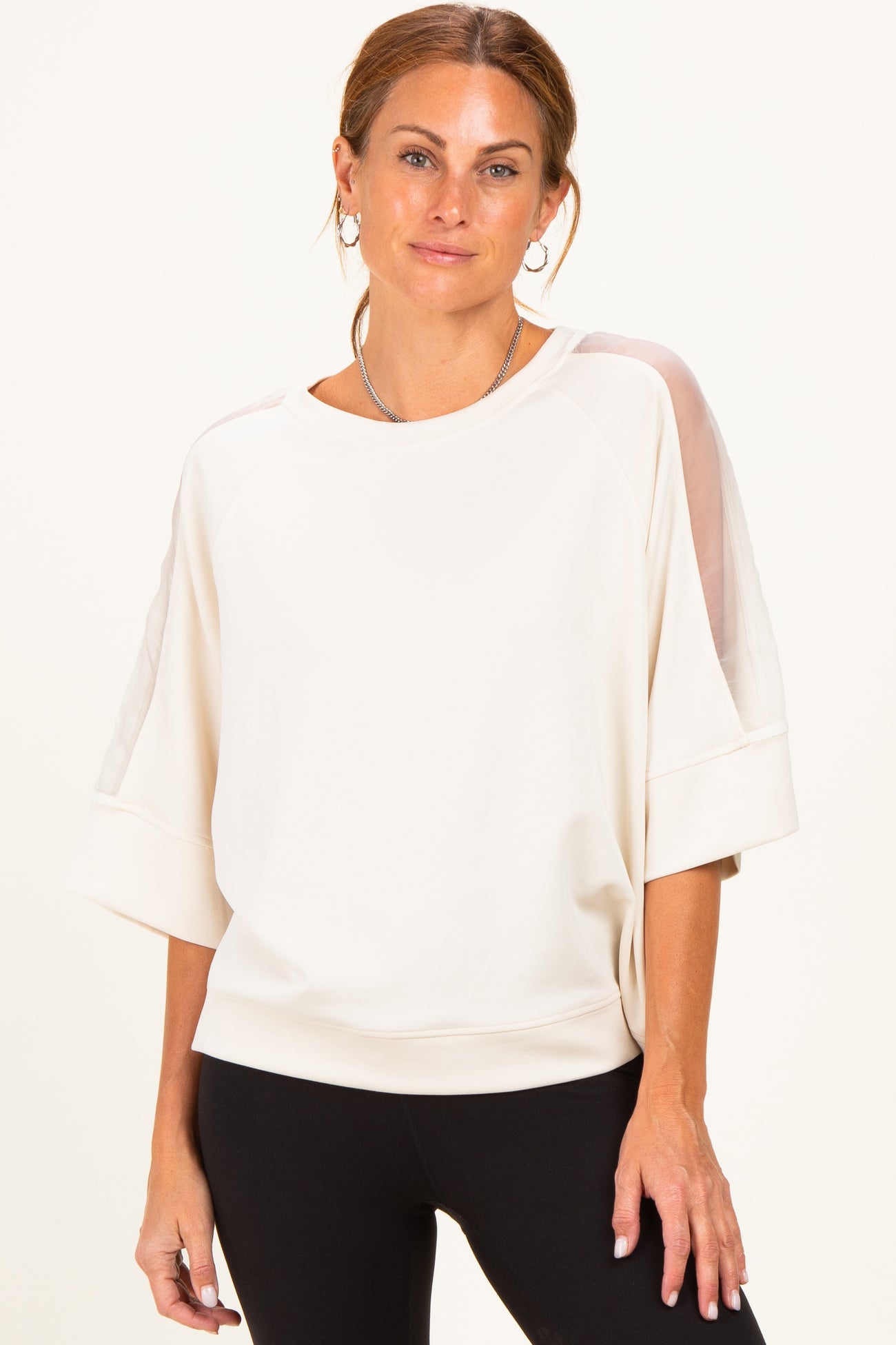 woman wearing a cream oversized sweatshirt with sheer details on sleeves and relaxed fit with black leggings