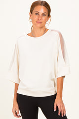 woman wearing a cream oversized sweatshirt with sheer details on sleeves and relaxed fit with black leggings