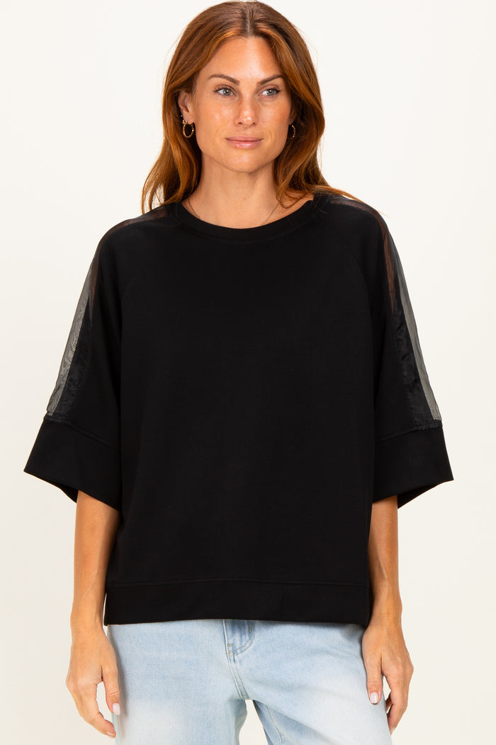 woman wearing a black oversized sweatshirt with sheer panels on the sleeves and a relaxed fit, styled with light blue jeans