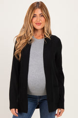 woman wearing a black maternity cardigan over a gray top and showing her baby bump while posing for the photo