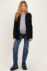 woman wearing a black cardigan over a gray top and blue jeans, showing her baby bump