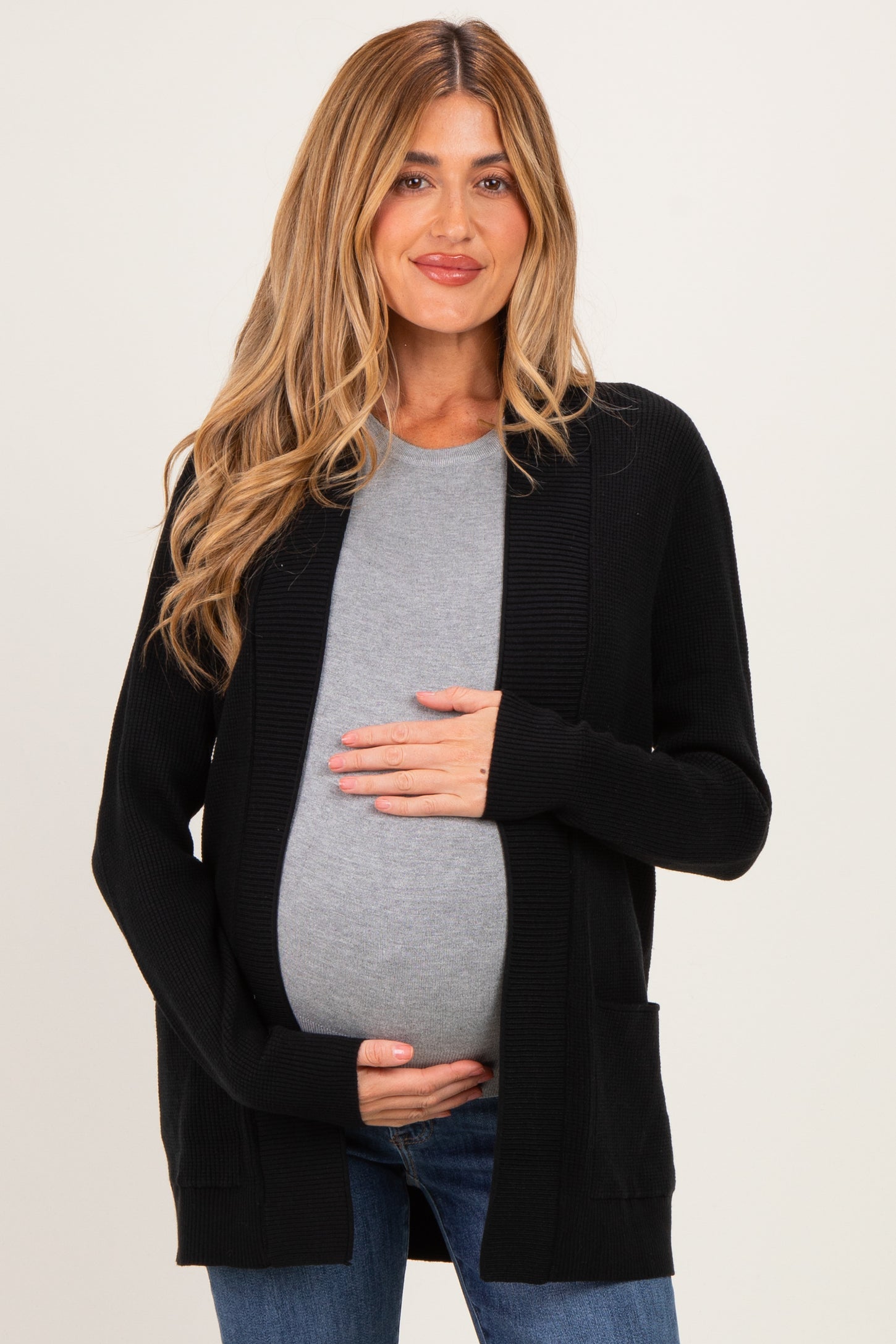 woman wearing a black long sleeve maternity cardigan over a grey top and holding her baby bump