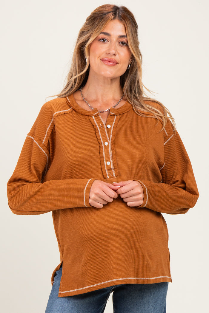 woman wearing a rusty orange maternity top with a button-front and ribbed texture, smiling at the camera