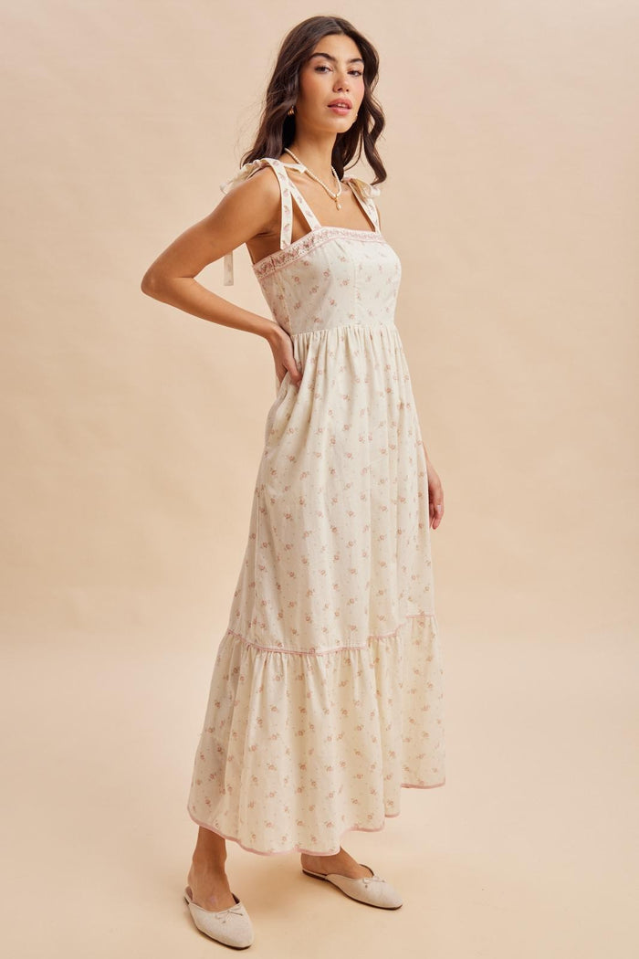 woman wearing a cream floral maxi dress with tie straps and ruffled hem, styled with slip-on shoes