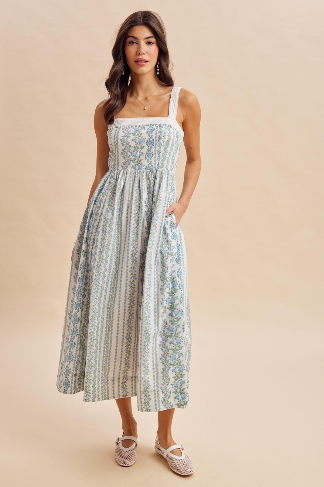 woman wearing a blue and white floral print maxi dress with adjustable straps and pockets