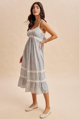 woman wearing a light blue floral maxi dress with lace details and adjustable straps, styled with white flats