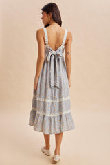 woman wearing a blue floral sundress with a deep back and bow detail, featuring a tiered ruffled hem