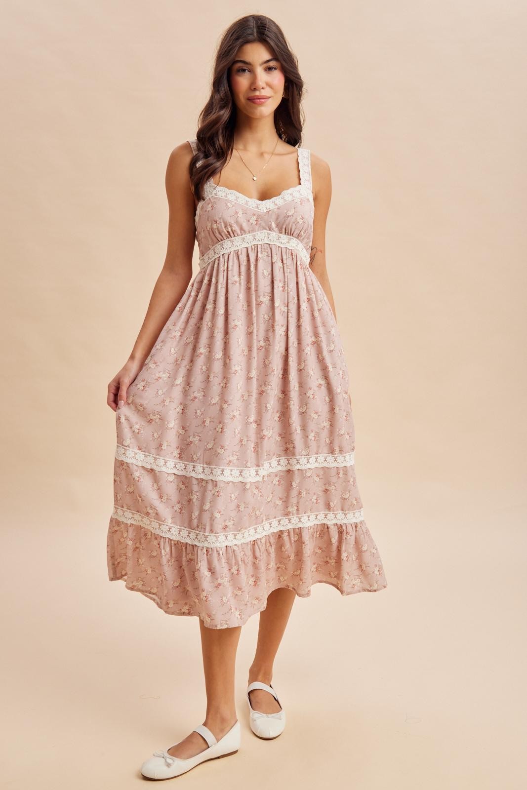 woman wearing a light pink floral maxi dress with lace detailing and a tiered hem