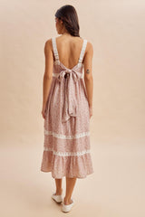 woman wearing a pink floral midi dress with a bow detail on the back and lace trim