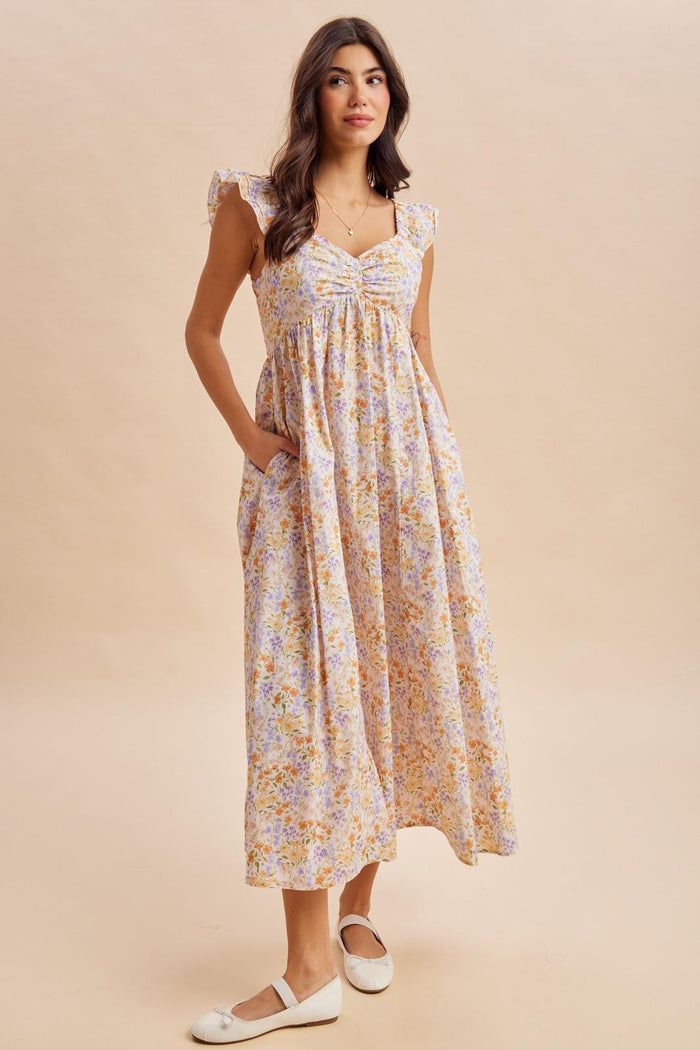 woman wearing a floral maxi dress with ruffled cap sleeves and pockets, standing on a neutral background