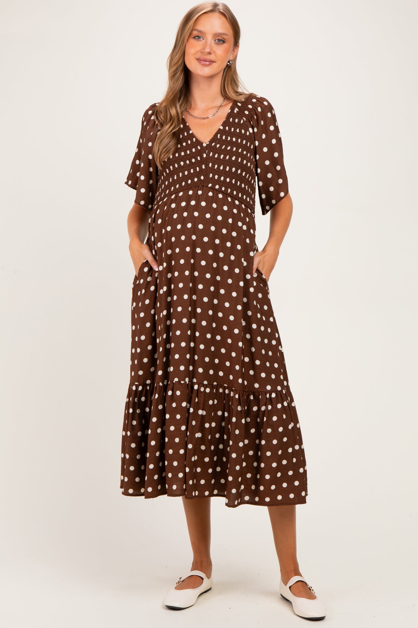 woman wearing a brown polka dot maternity dress with short sleeves and a tiered skirt, holding her baby bump