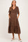woman wearing a brown polka dot maternity dress with short sleeves and a tiered skirt, holding her baby bump