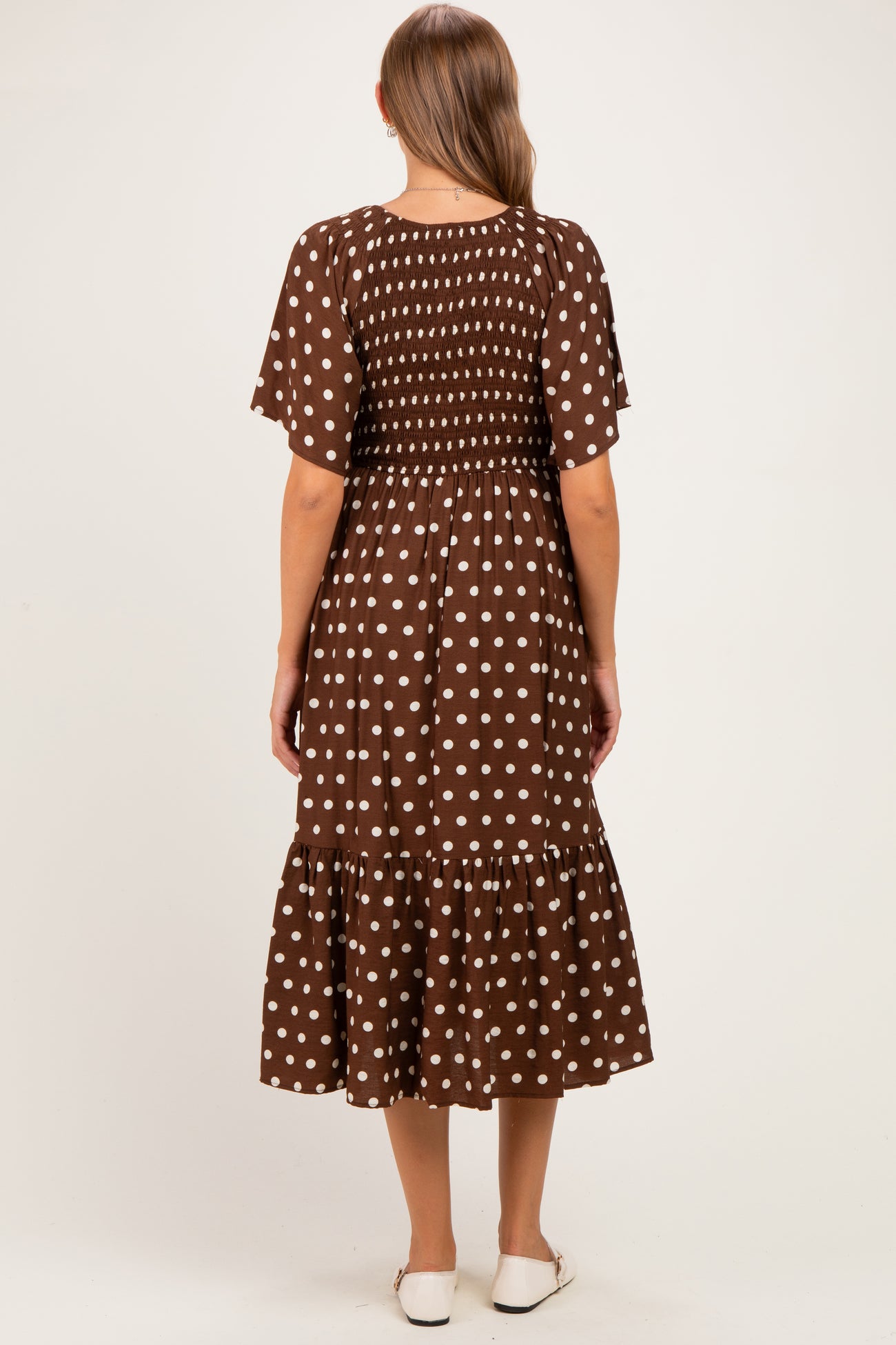 woman wearing a brown polka dot maternity dress with short sleeves and a tiered skirt, showing a baby bump from the back
