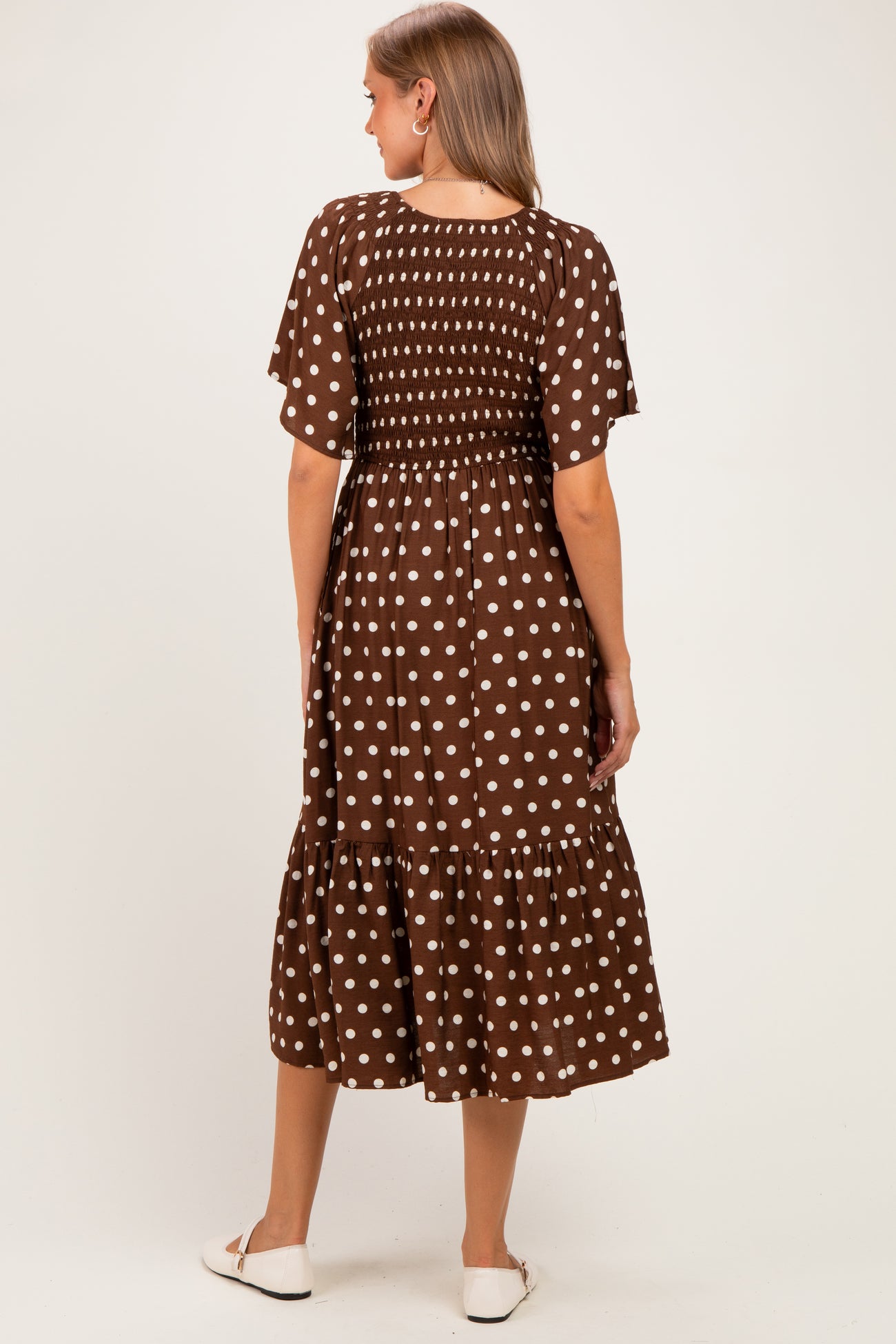 woman wearing a brown polka dot maternity dress with short flutter sleeves and a tiered skirt, showing a baby bump from the back