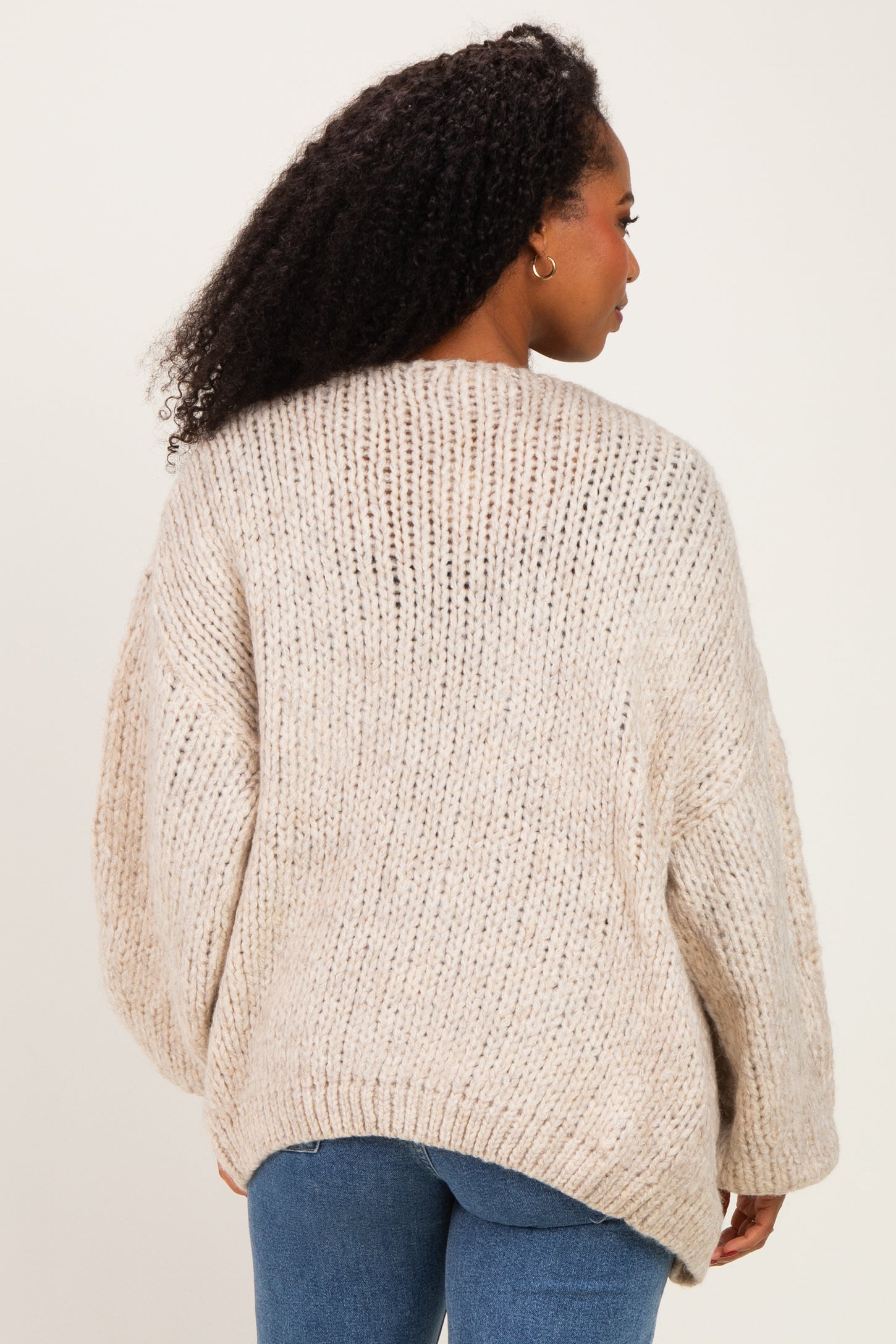 woman wearing a chunky knit beige sweater with a relaxed fit and dropped shoulders, viewed from the back