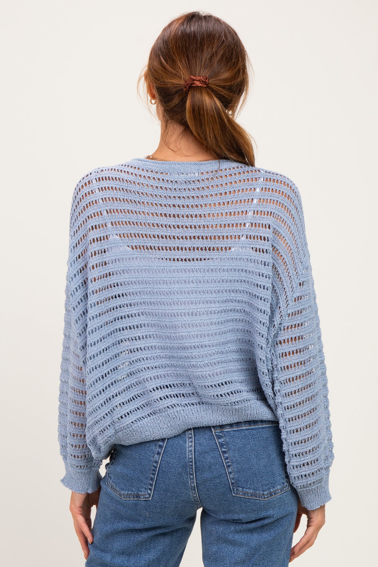 woman wearing a light blue open-knit sweater with a relaxed fit and long sleeves, styled with high-waisted jeans