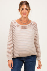 woman wearing a light beige open knit maternity sweater with a visible baby bump and casual jeans