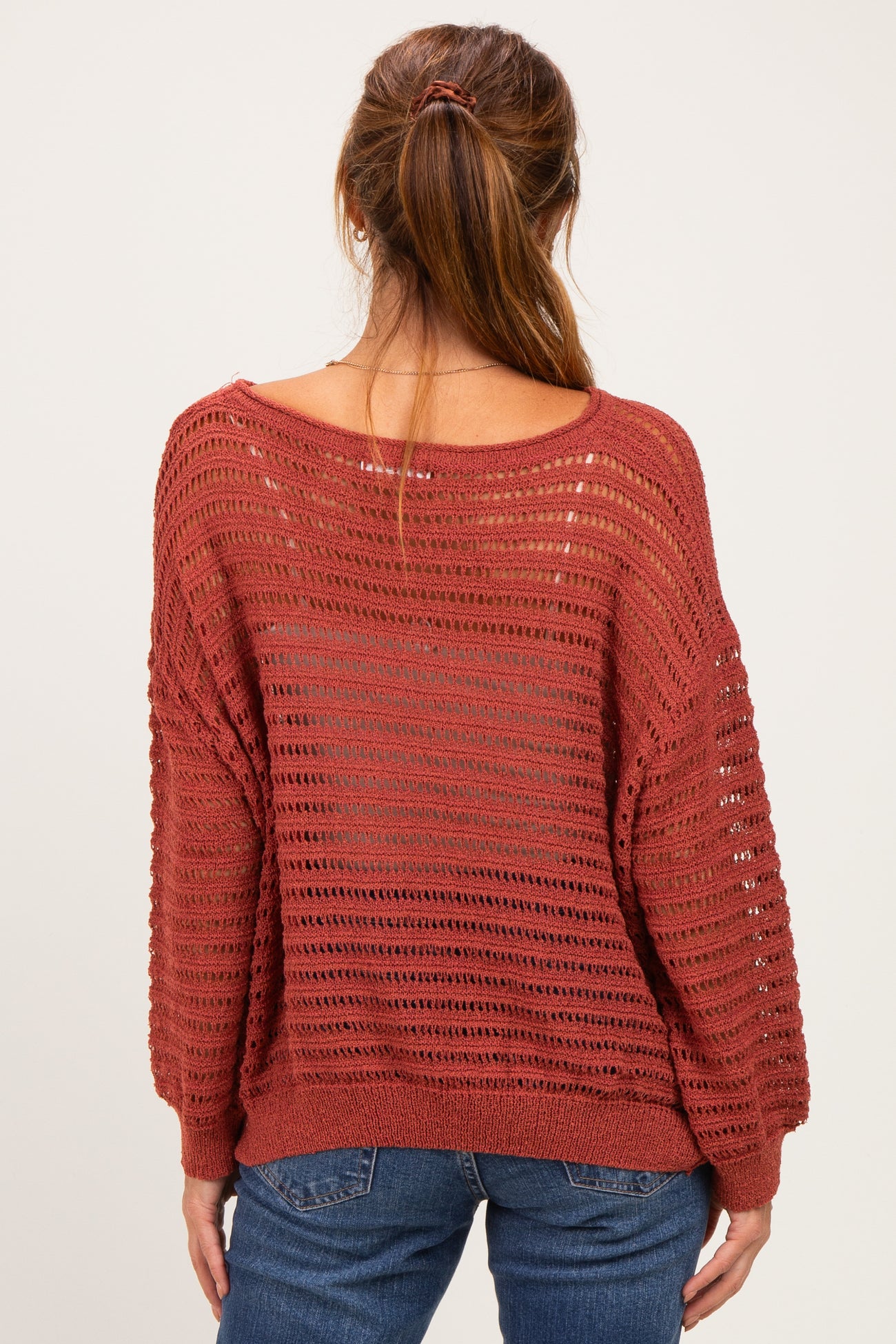 woman wearing a rust-colored loose-knit sweater with a wide neckline and long sleeves, viewed from the back