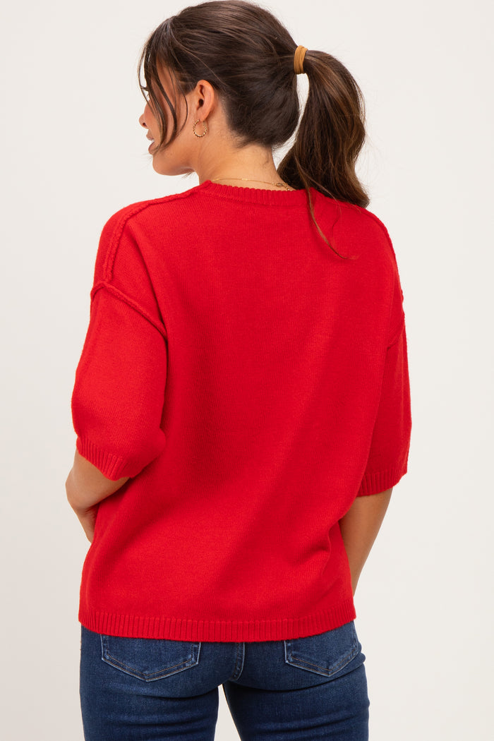 woman wearing a red short sleeve maternity sweater with a relaxed fit, styled with blue jeans and a ponytail