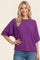 woman wearing a purple short sleeve sweater with a relaxed fit and smiling at the camera