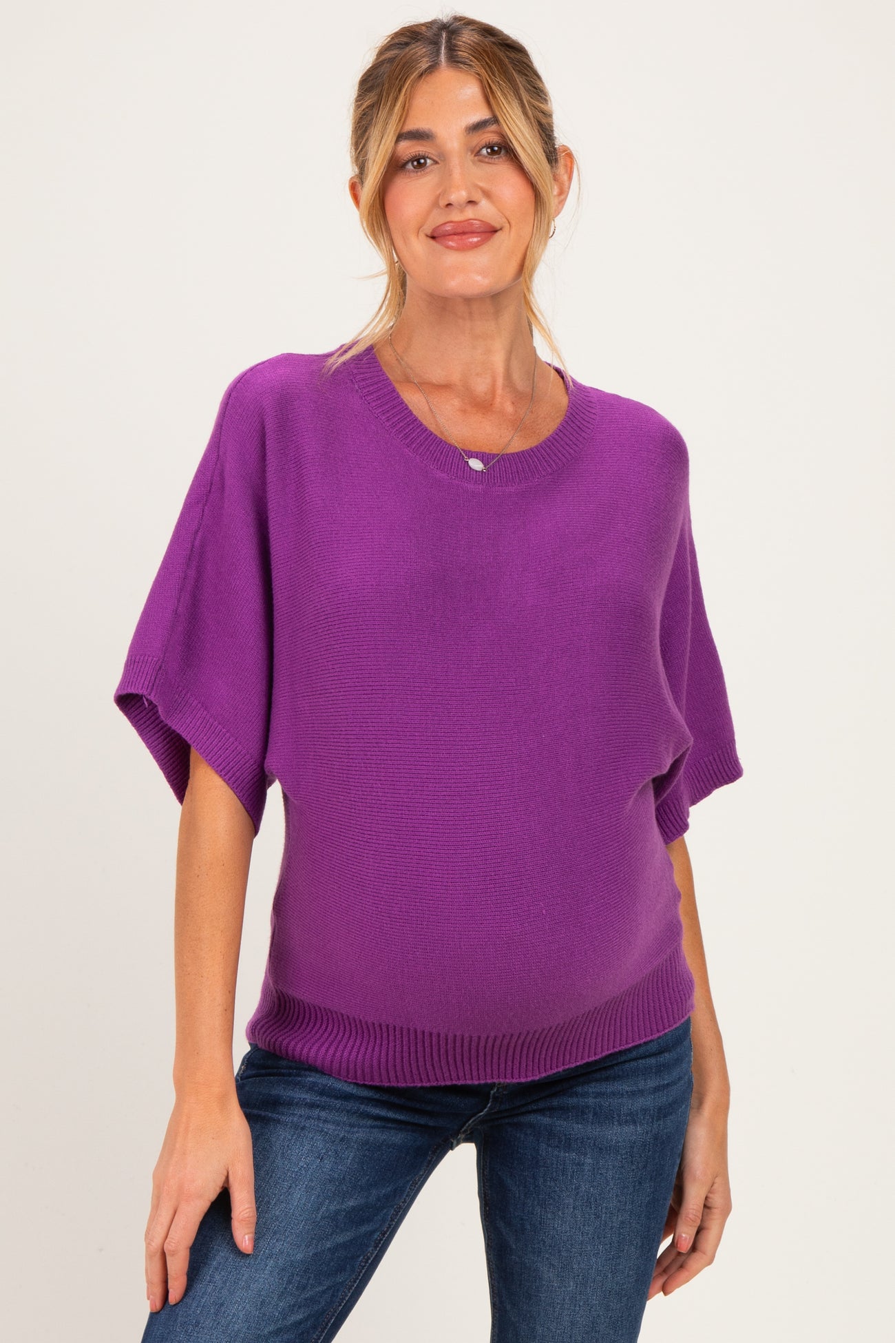 woman wearing a bright purple short sleeve maternity sweater and showing her baby bump with a relaxed fit