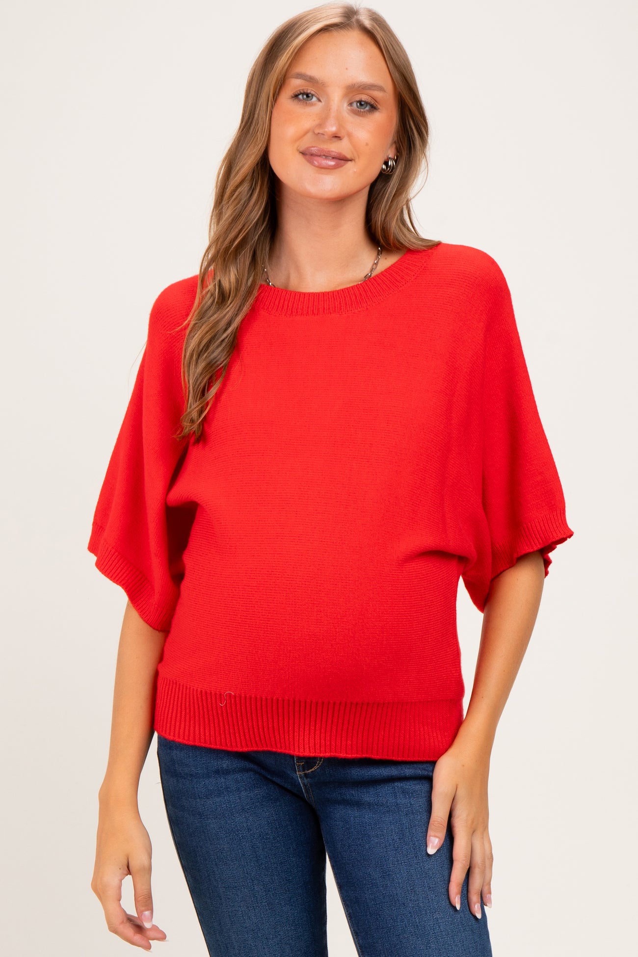 woman wearing a bright red short sleeve maternity sweater and showing her baby bump