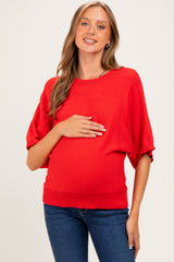woman wearing a bright red maternity sweater with batwing sleeves and holding her baby bump