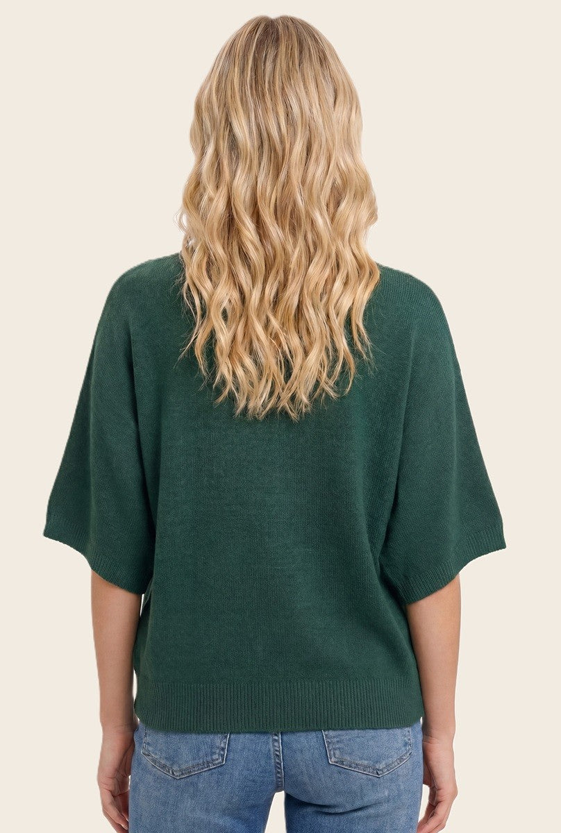 woman wearing a dark green oversized sweater with short sleeves, shown from the back, styled with casual denim jeans