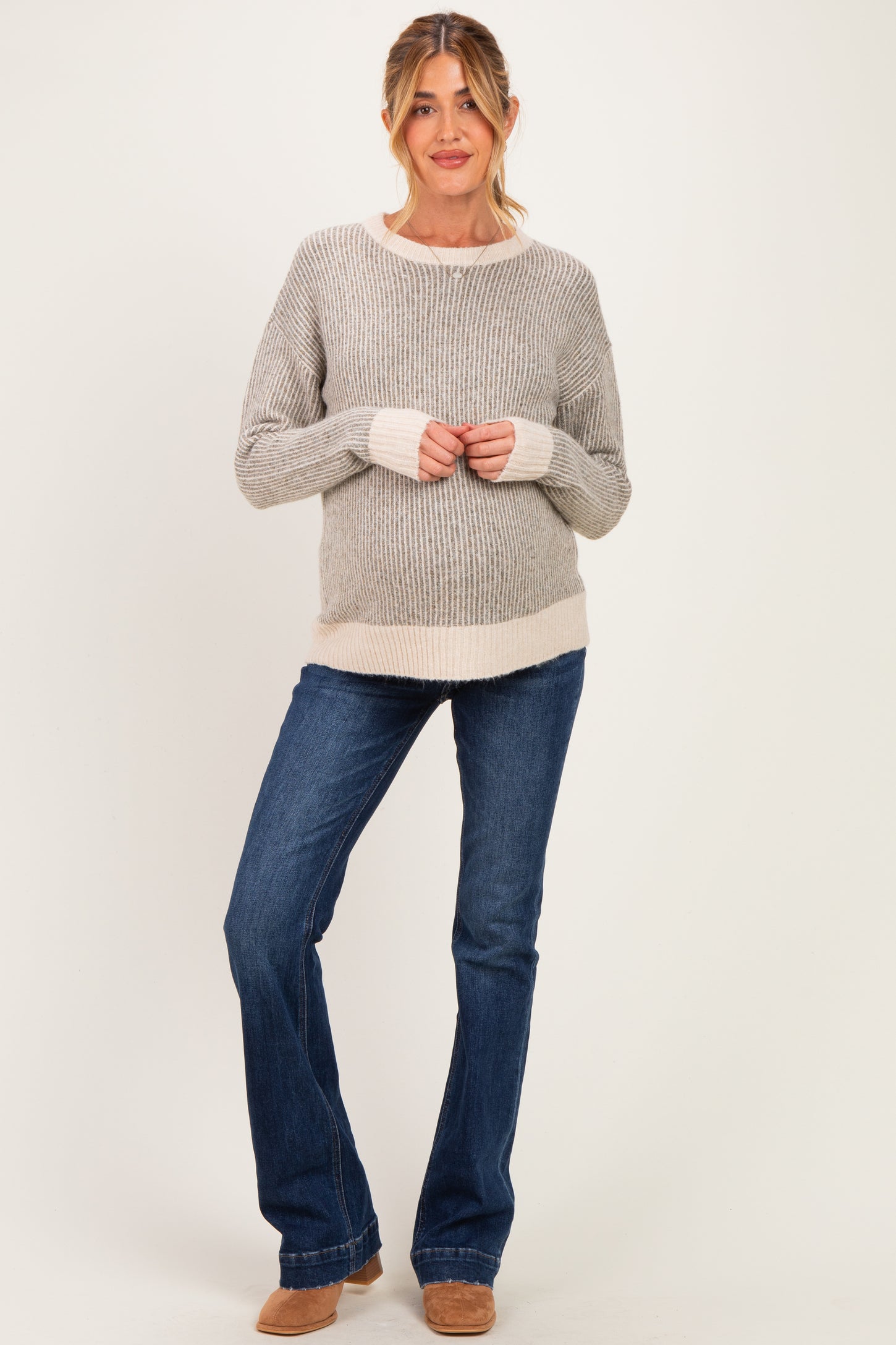 woman wearing a gray and cream striped maternity sweater with long sleeves and holding her baby bump, paired with flared jeans