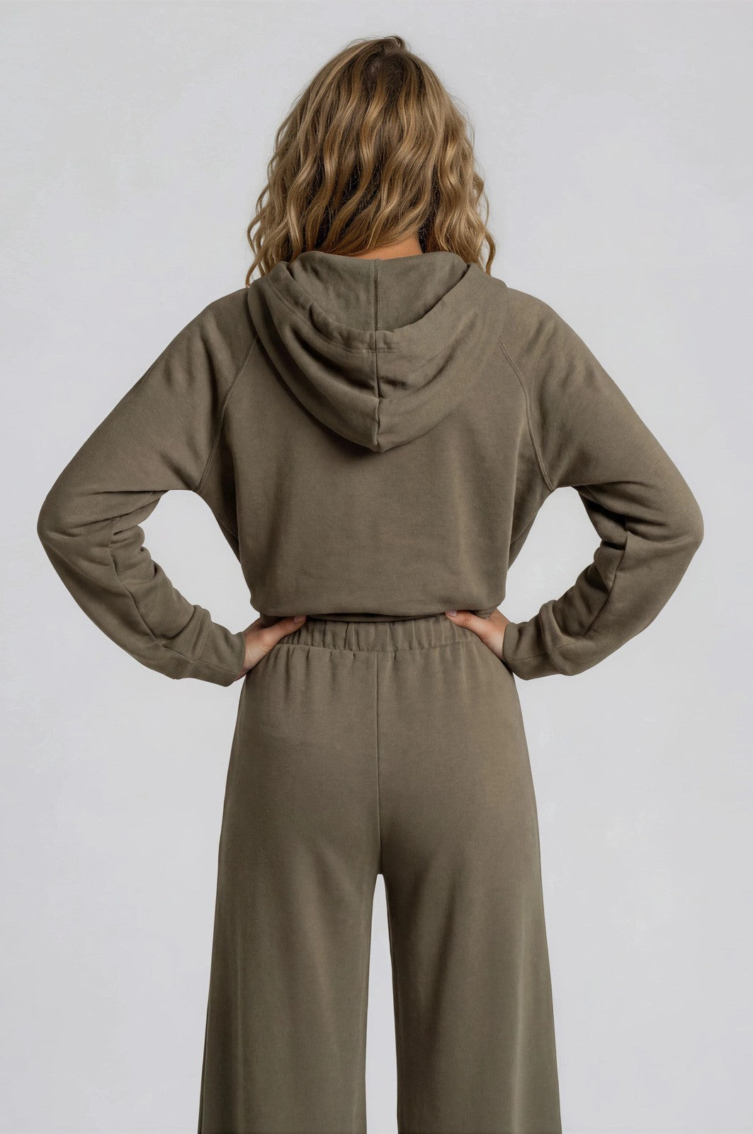 woman wearing a cropped olive green hoodie with a hood and matching high-waisted wide-leg pants from the back