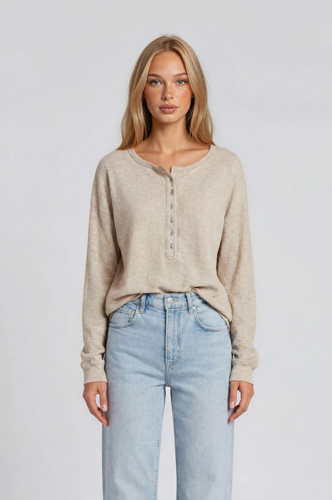 woman wearing a light beige long sleeve henley top with buttons, paired with light wash high-waisted jeans