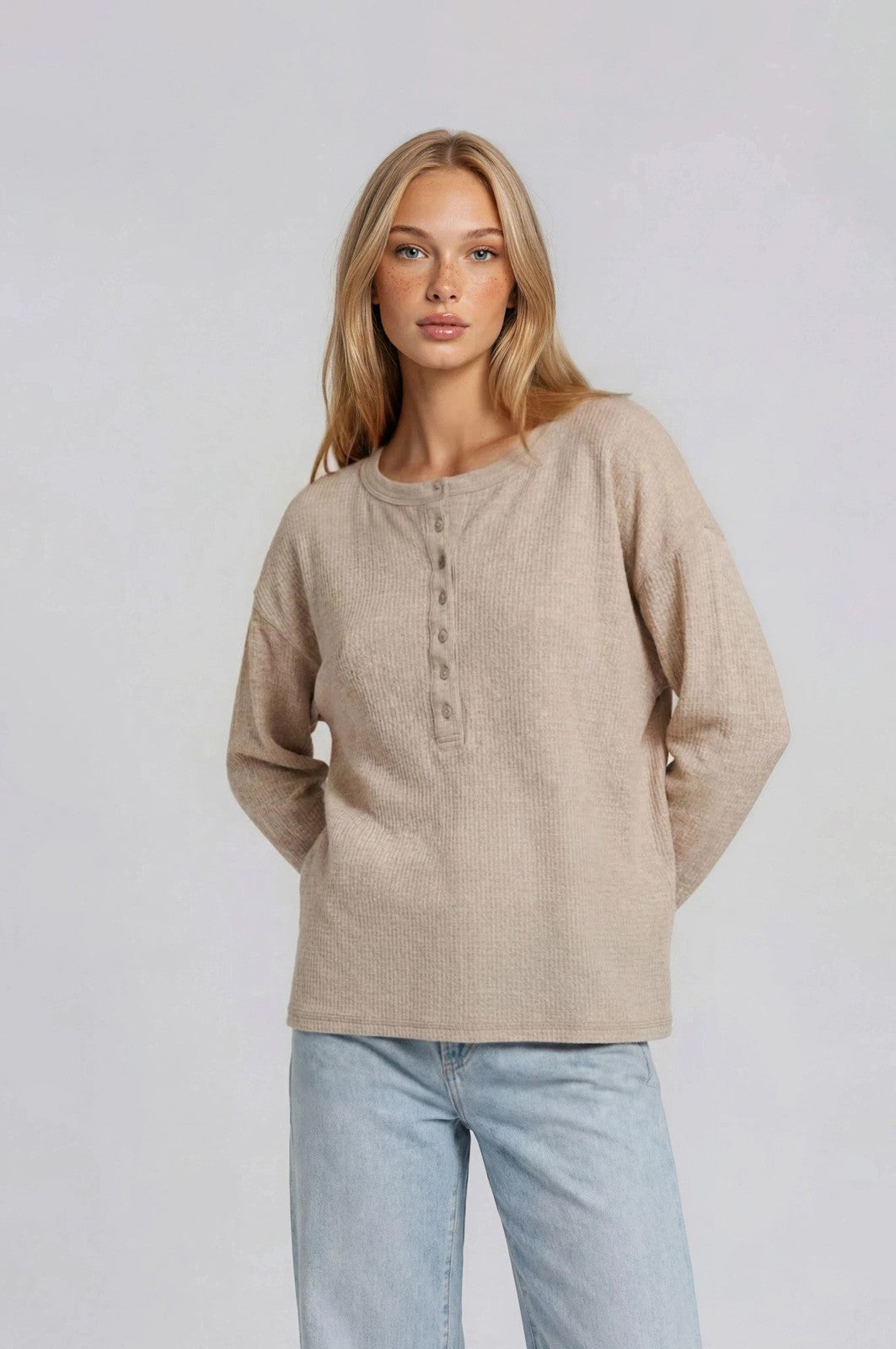 woman wearing a beige long sleeve henley top with buttons and relaxed fit, paired with light blue jeans