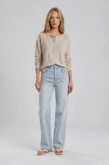 woman wearing a beige long sleeve henley top paired with light blue wide leg jeans and white flip flops