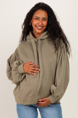 woman wearing an olive green oversized maternity hoodie and holding her baby bump