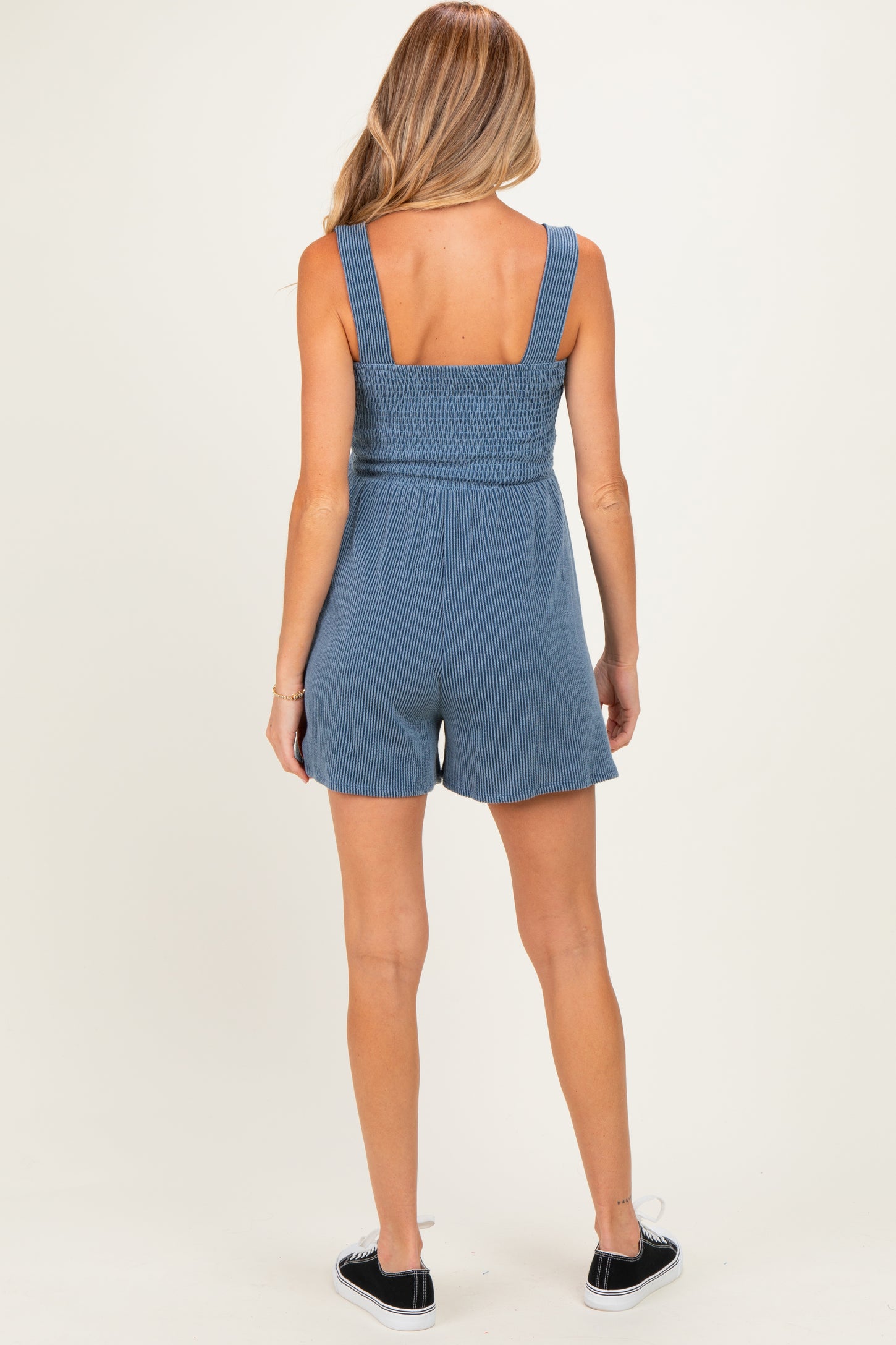 woman wearing a blue striped maternity romper with a smocked bodice, showing the back view